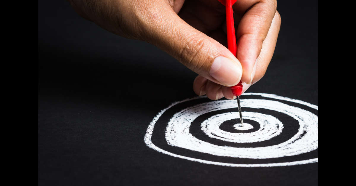 A hand placing a dart in the center of a target.