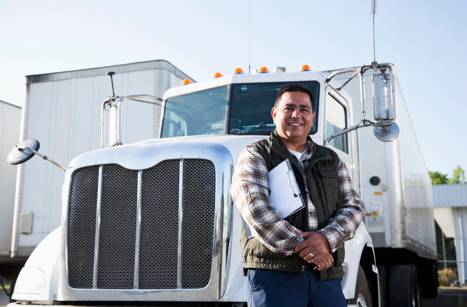A driver holding a clipboard and smiling in front of his truck.